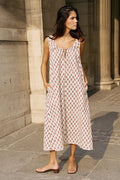 Woman standing beside classical stone columns wearing the Daughters of India Sundress Midi in Peony, a sleeveless pink floral block print cotton midi dress with tie neckline