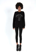Model wearing Carbon Jeans Talk Top black oversized sweatshirt with white graphic text, skinny jeans, and black boots.