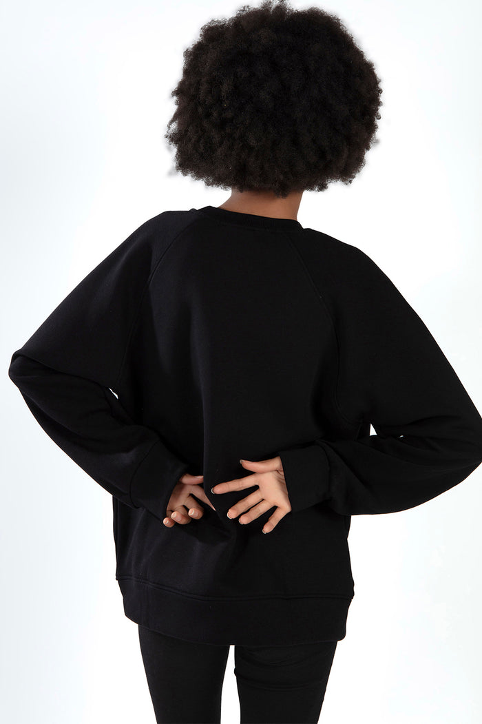 Back view of a model with an afro wearing a Carbon Jeans oversized black crewneck sweatshirt with raglan sleeves.