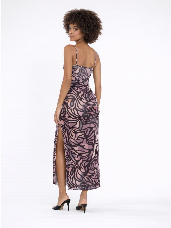 A model showcases a form-fitting, patterned dress with a thigh-high slit, paired with black heels.