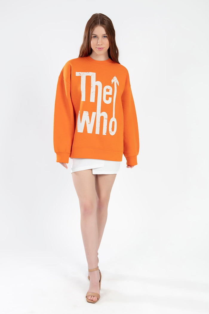 Model wearing orange The Who graphic sweatshirt, oversized crewneck knit top with white logo, white skirt, and tan heels.