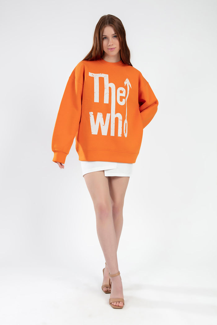 Model in orange The Who graphic sweatshirt and white mini skirt, a trendy knit top for streetwear fashion.