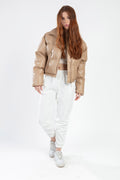 Model wearing Thea beige vegan leather puffer coat with white joggers and sneakers, street style fashion.