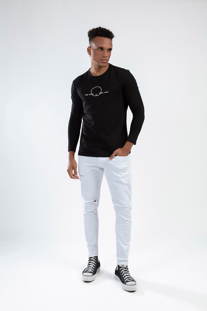 Model in Carbon Jeans black long-sleeve Time Never Shirt, white distressed denim jeans, and black sneakers.