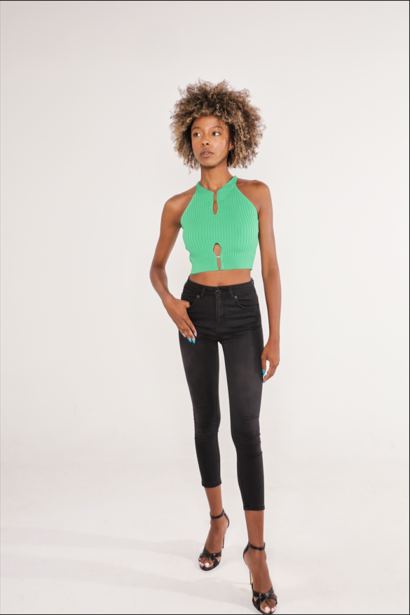 Model wearing the Tori Top, a green ribbed halter crop top with keyhole cutouts, paired with black skinny jeans.