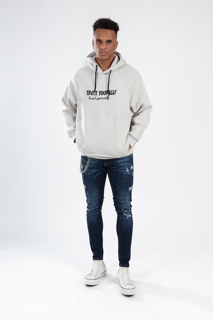 Model in oversized light grey Trust Yourself graphic hoodie, distressed skinny jeans, and white high-top sneakers.