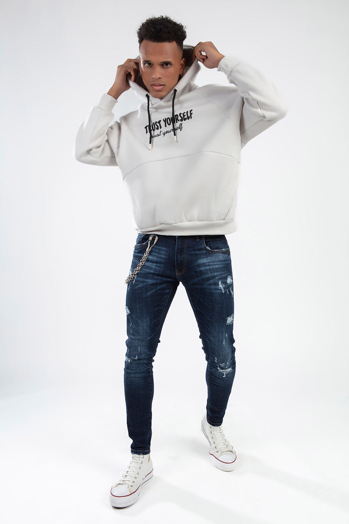 Model in Oversized Light Grey 'Trust Yourself' Graphic Hoodie, distressed denim, and white sneakers streetwear vibe.