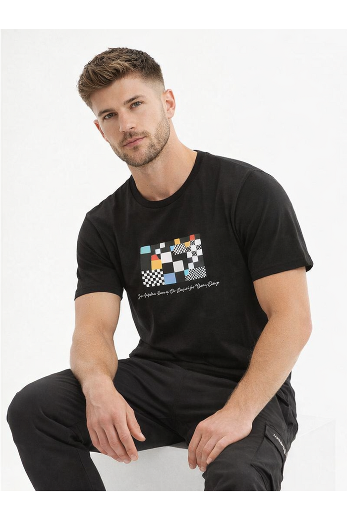 A man wearing a black t-shirt with a colorful geometric design sits casually, showcasing a relaxed style.
