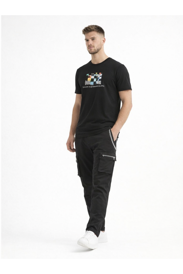A man stands confidently in a black graphic t-shirt and black cargo pants, paired with white sneakers.