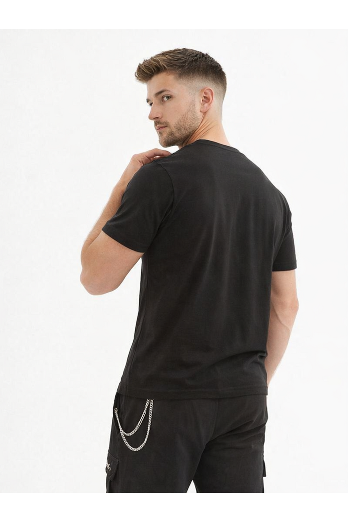 A man with short hair wearing a black t-shirt and cargo pants, looking back over his shoulder.
