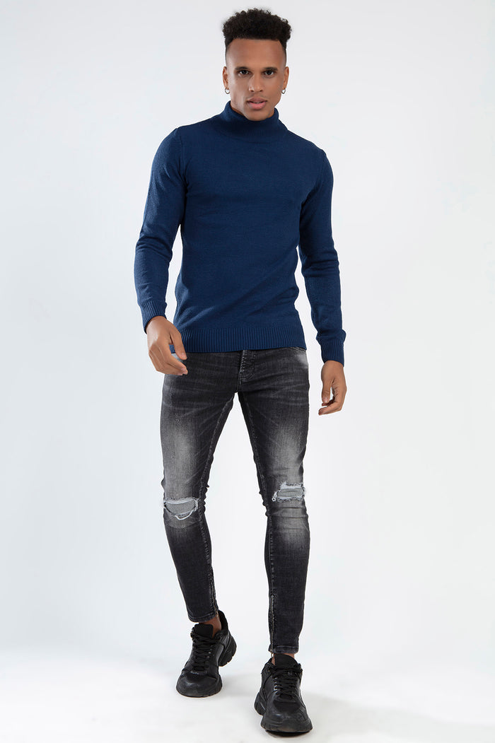 Man in a navy blue Tyson knit turtleneck sweater paired with distressed black jeans and sneakers.