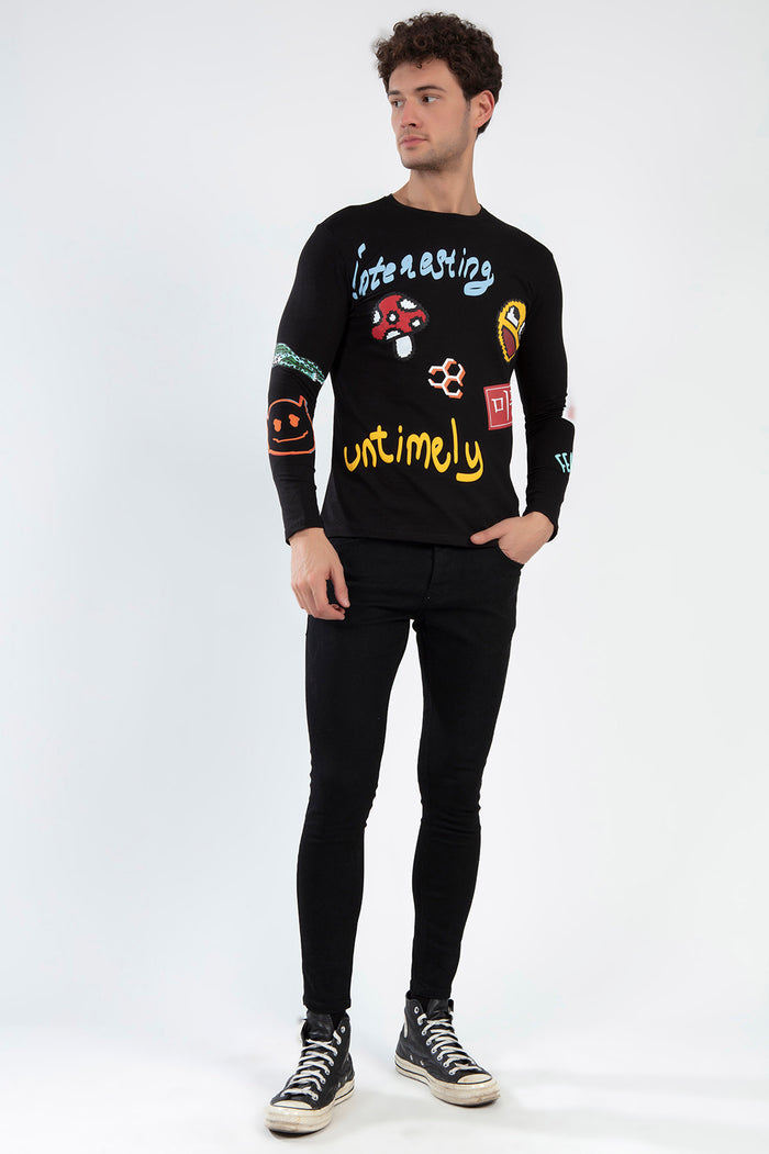 Model wearing Untimely black long sleeve graphic shirt with pixel art patches and streetwear text on a white studio background.