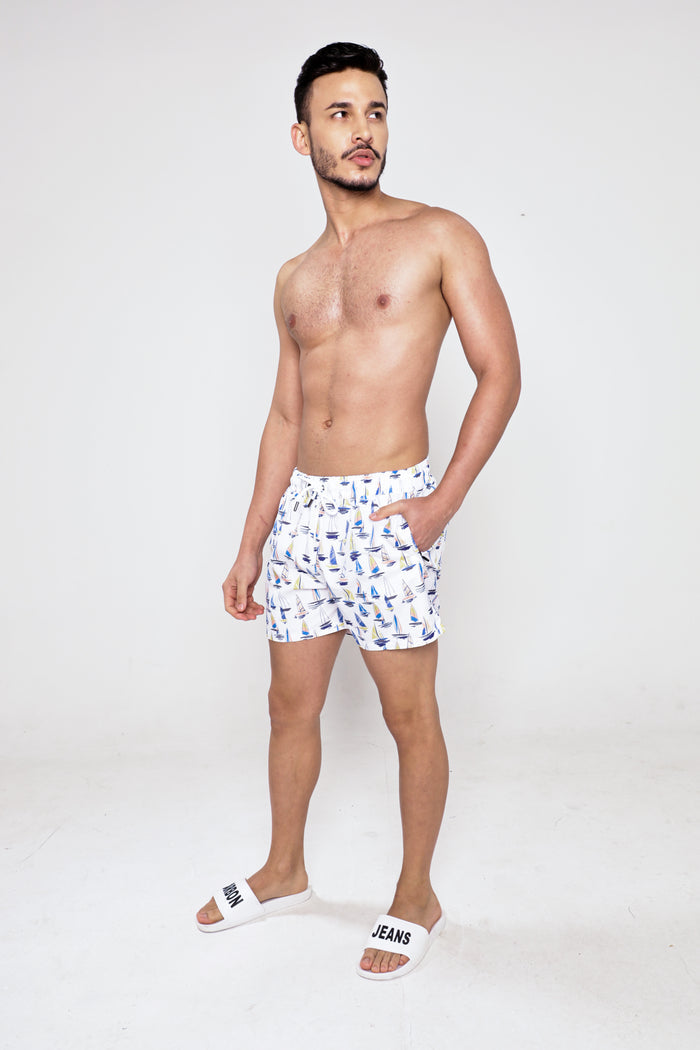 Model wearing Walker sailboat patterned swim trunks and white slides, showcasing a trendy men's summer beachwear look.